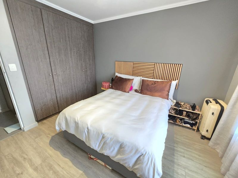 A well-maintained bedroom featuring modern laminate flooring, neutral grey walls, and a large built-in wardrobe with wood-grain finish.