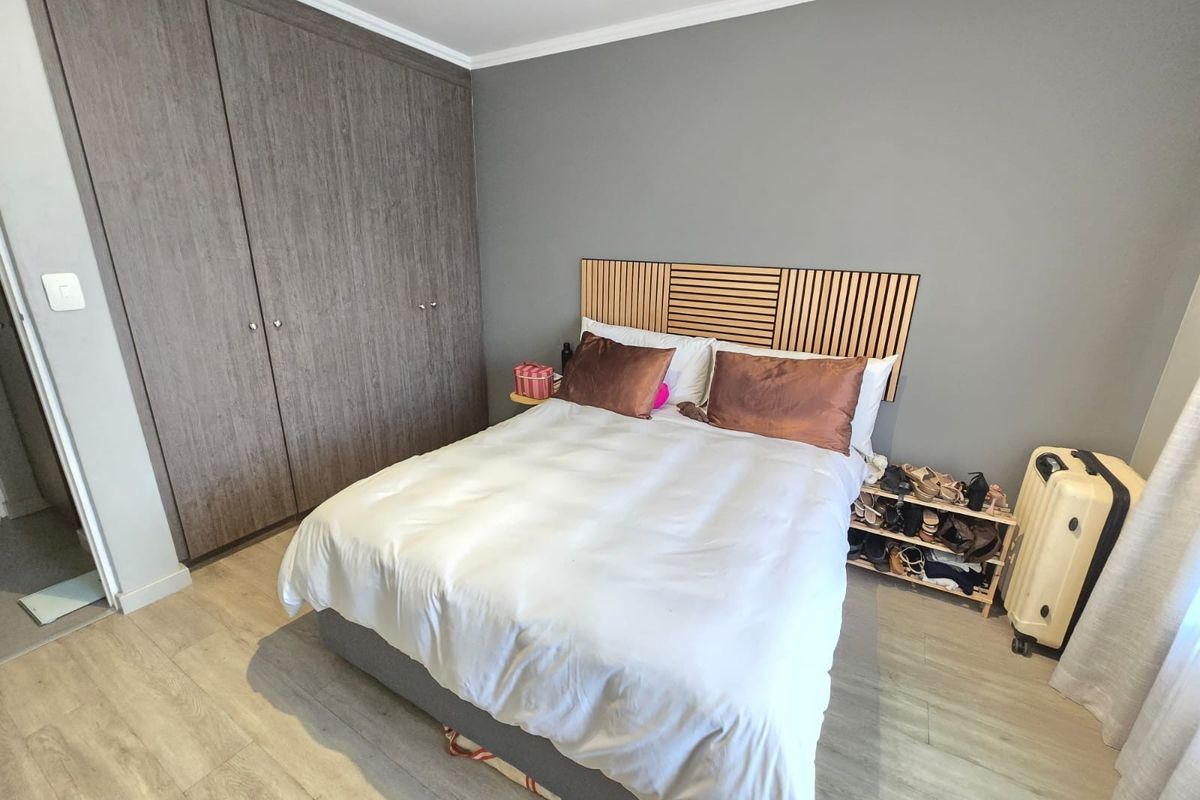 A well-maintained bedroom featuring modern laminate flooring, neutral grey walls, and a large built-in wardrobe with wood-grain finish.