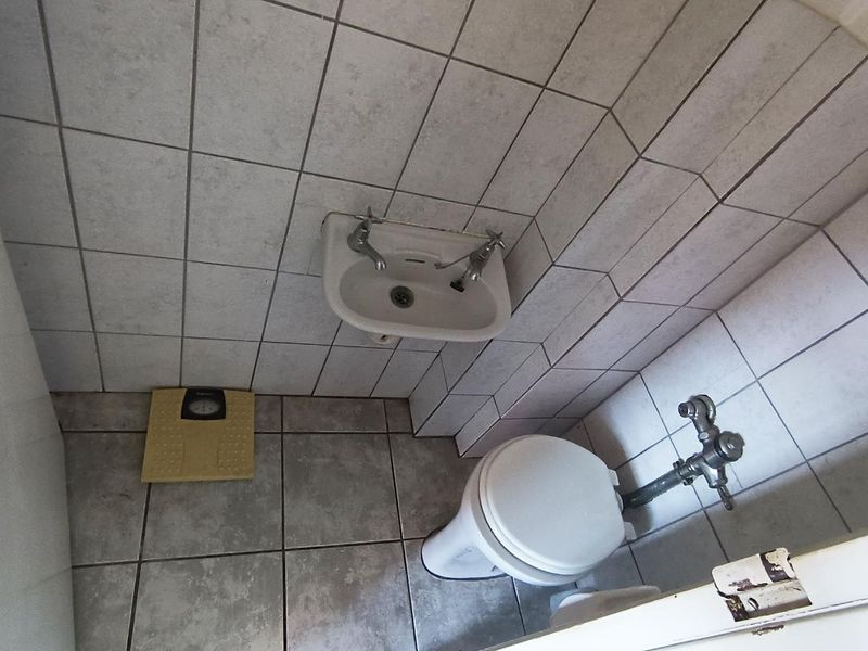 A compact bathroom featuring a wall-mounted basin and toilet with full-height ceramic wall tiling and tiled flooring.