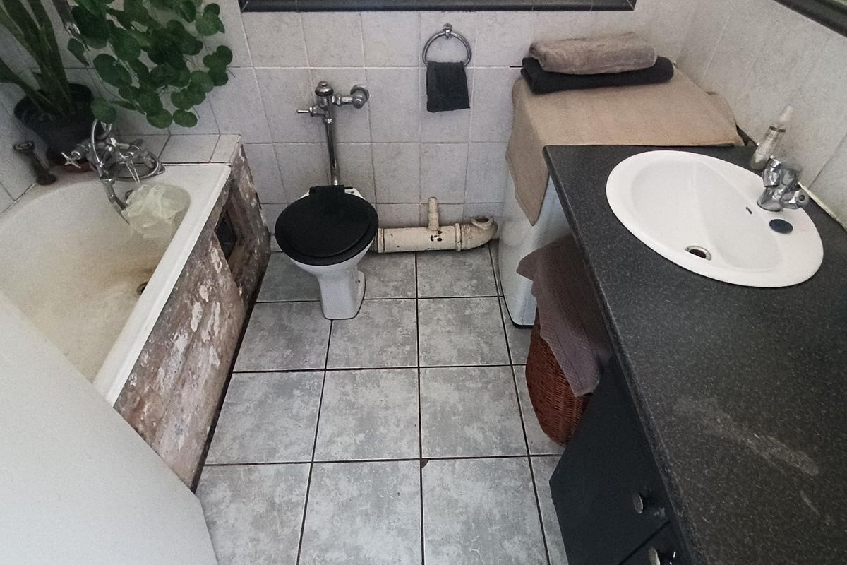 A dated bathroom featuring a bathtub with damaged side paneling, a toilet with exposed plumbing, and a vanity sink with a dark countertop.
