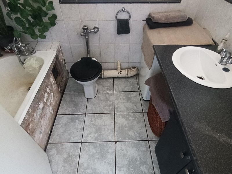A dated bathroom featuring a bathtub with damaged side paneling, a toilet with exposed plumbing, and a vanity sink with a dark countertop.