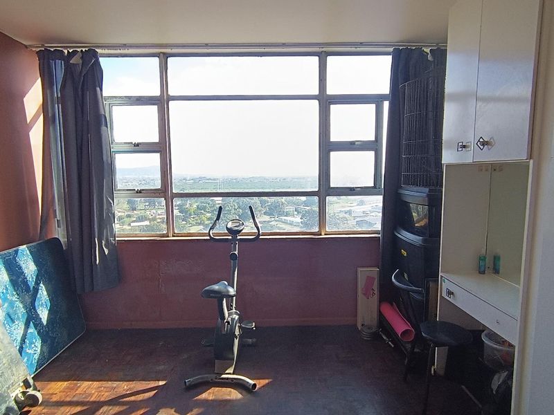 A bedroom featuring large windows with expansive views, built-in cabinetry, and parquet flooring, offering a functional space with potential for modernization.