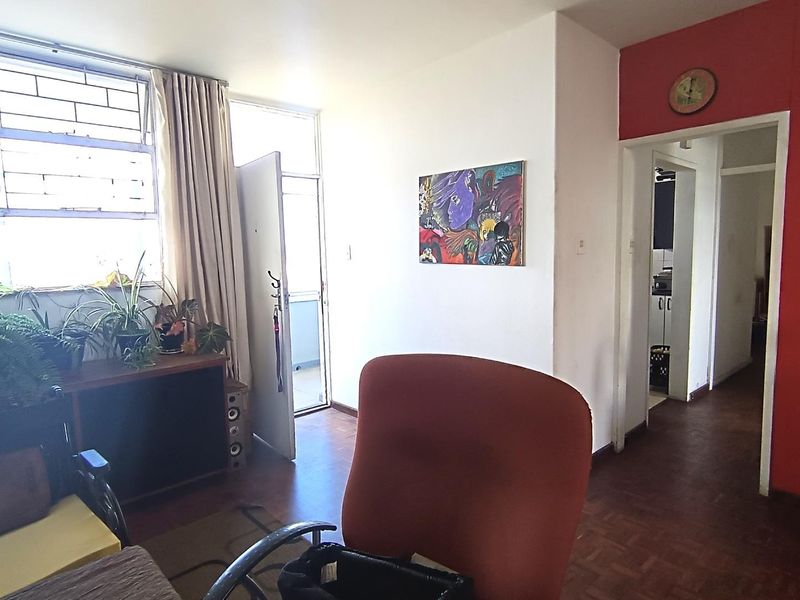 Living room area featuring parquet flooring, large windows with security bars, and access to an adjacent hallway and balcony.