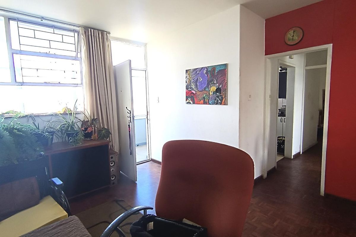 Living room area featuring parquet flooring, large windows with security bars, and access to an adjacent hallway and balcony.