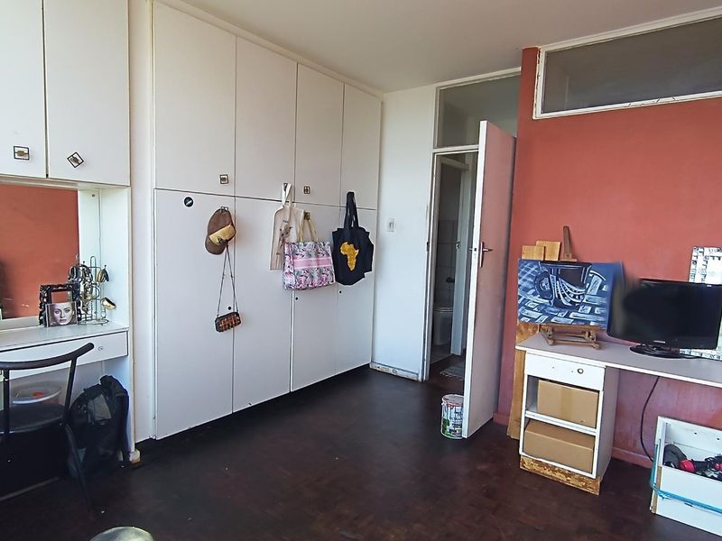 Bedroom featuring extensive built-in cupboard storage, a integrated vanity unit, and dark flooring, offering a functional layout with potential for cosmetic updates.
