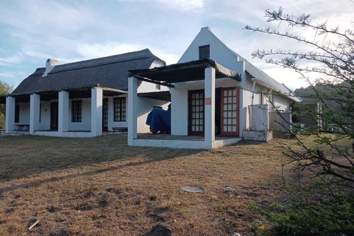 Rear view of a traditional farmhouse featuring a thatched roof, covered patio areas, and external water storage tanks on a rural property.