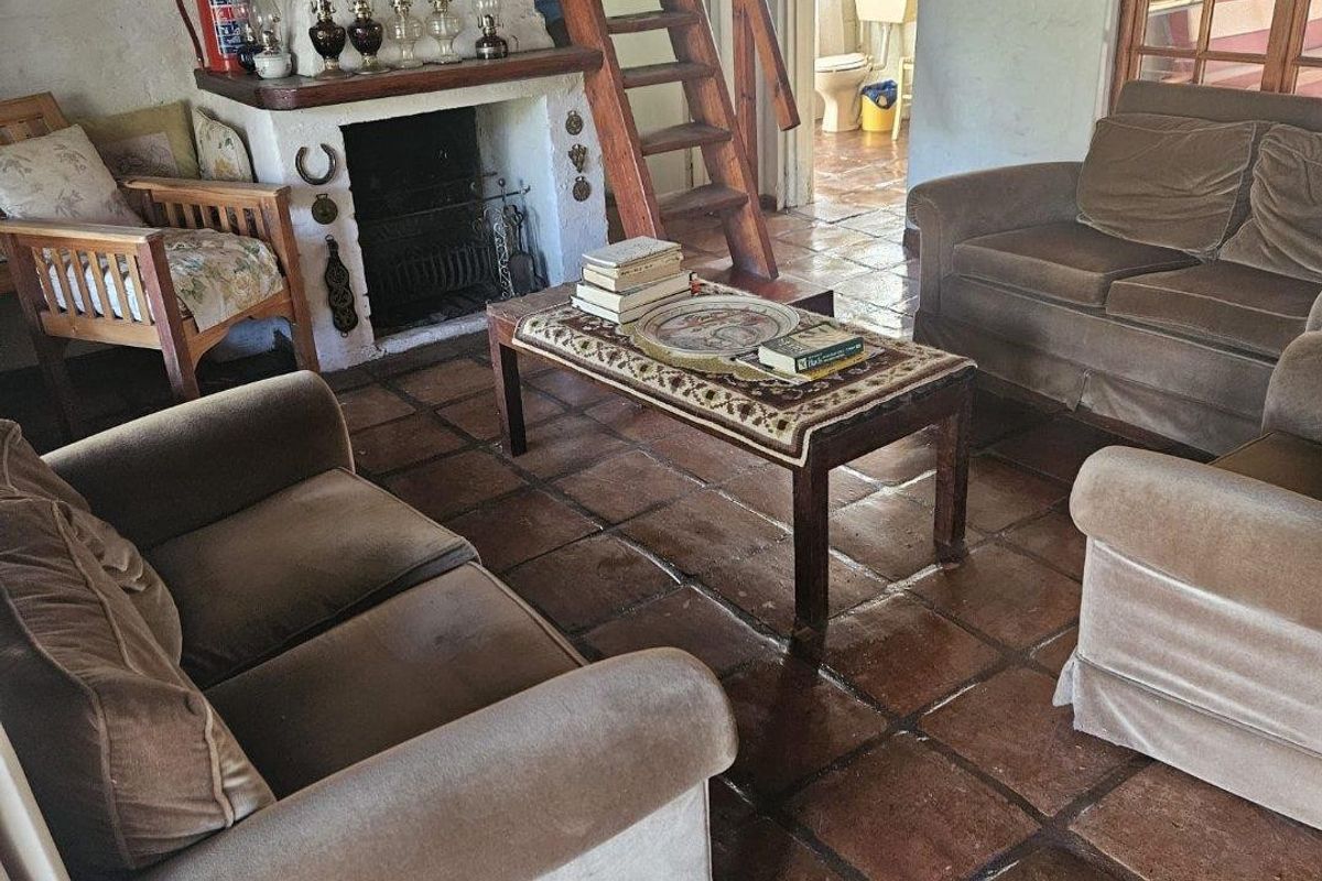 Rustic living room featuring a traditional fireplace, terracotta tiled flooring, and a wooden ladder leading to an upper level.