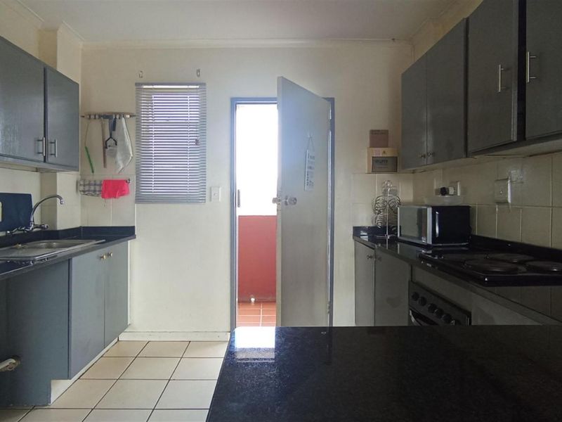 A functional kitchen featuring dark grey cabinetry, granite countertops, built-in oven and hob, and tiled flooring with direct access to an outdoor area.