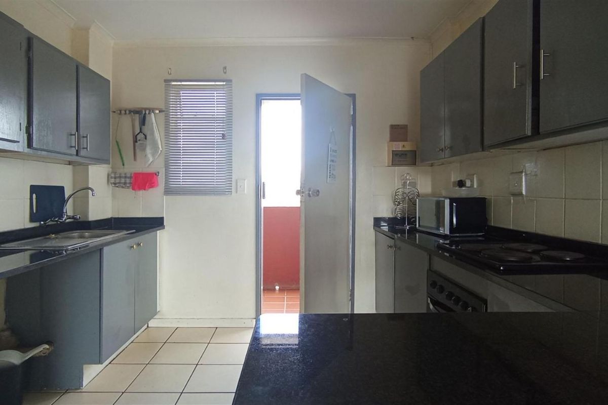 A functional kitchen featuring dark grey cabinetry, granite countertops, built-in oven and hob, and tiled flooring with direct access to an outdoor area.
