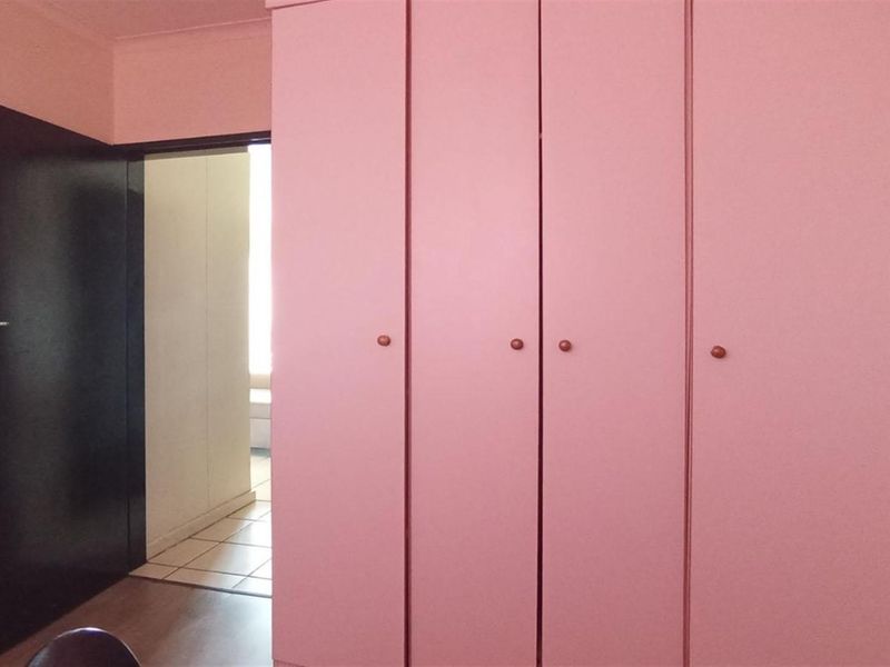 A bedroom interior featuring built-in pink cupboards and a dark interior door leading to an adjacent tiled hallway.