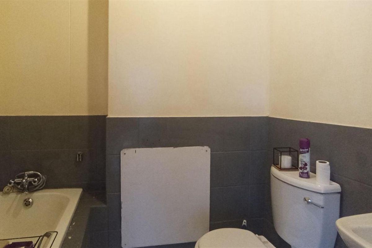 A functional bathroom featuring a bathtub, toilet, and washbasin with grey tiled splashbacks, requiring minor repairs to the wall paneling.