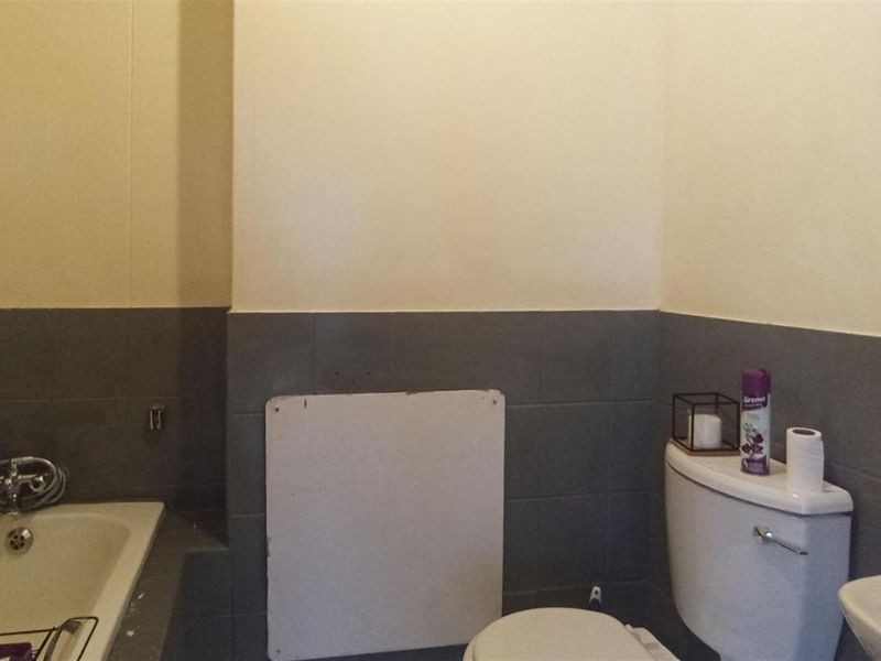 A functional bathroom featuring a bathtub, toilet, and washbasin with grey tiled splashbacks, requiring minor repairs to the wall paneling.