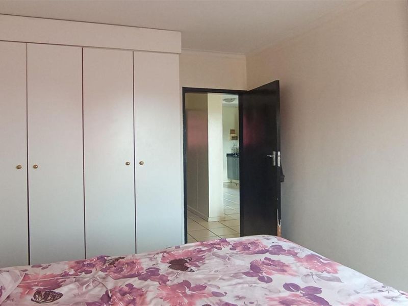 A bedroom featuring white built-in cupboards and a doorway leading to an adjacent tiled living area.