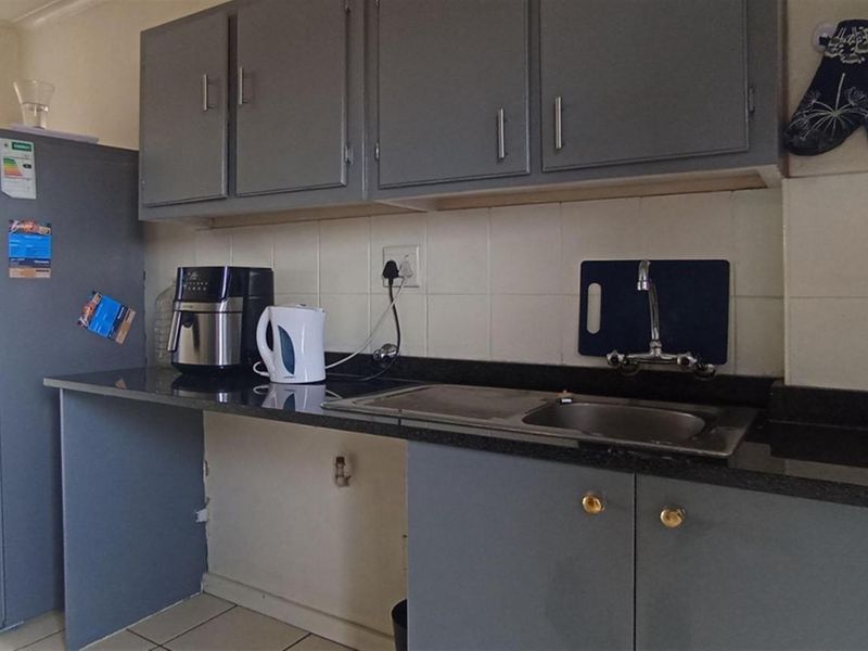 A functional kitchen featuring grey cabinetry, granite countertops, a stainless steel double sink, and tiled flooring.