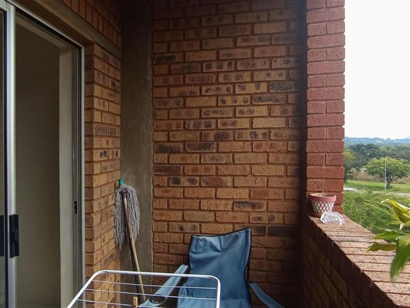 A covered balcony featuring exposed brick walls and a brick balustrade, offering an elevated view of the surrounding landscape.