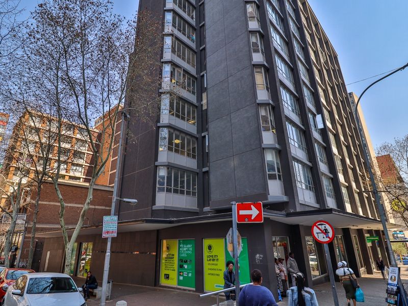 A multi-story commercial building featuring a dark facade, large windows, and ground-level retail space situated on a busy urban street corner.