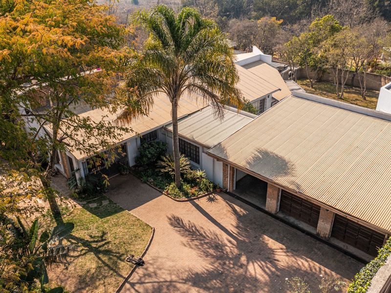 Aerial view of the property showcasing the main house, paved driveway, multi-car garage, and established garden surroundings.