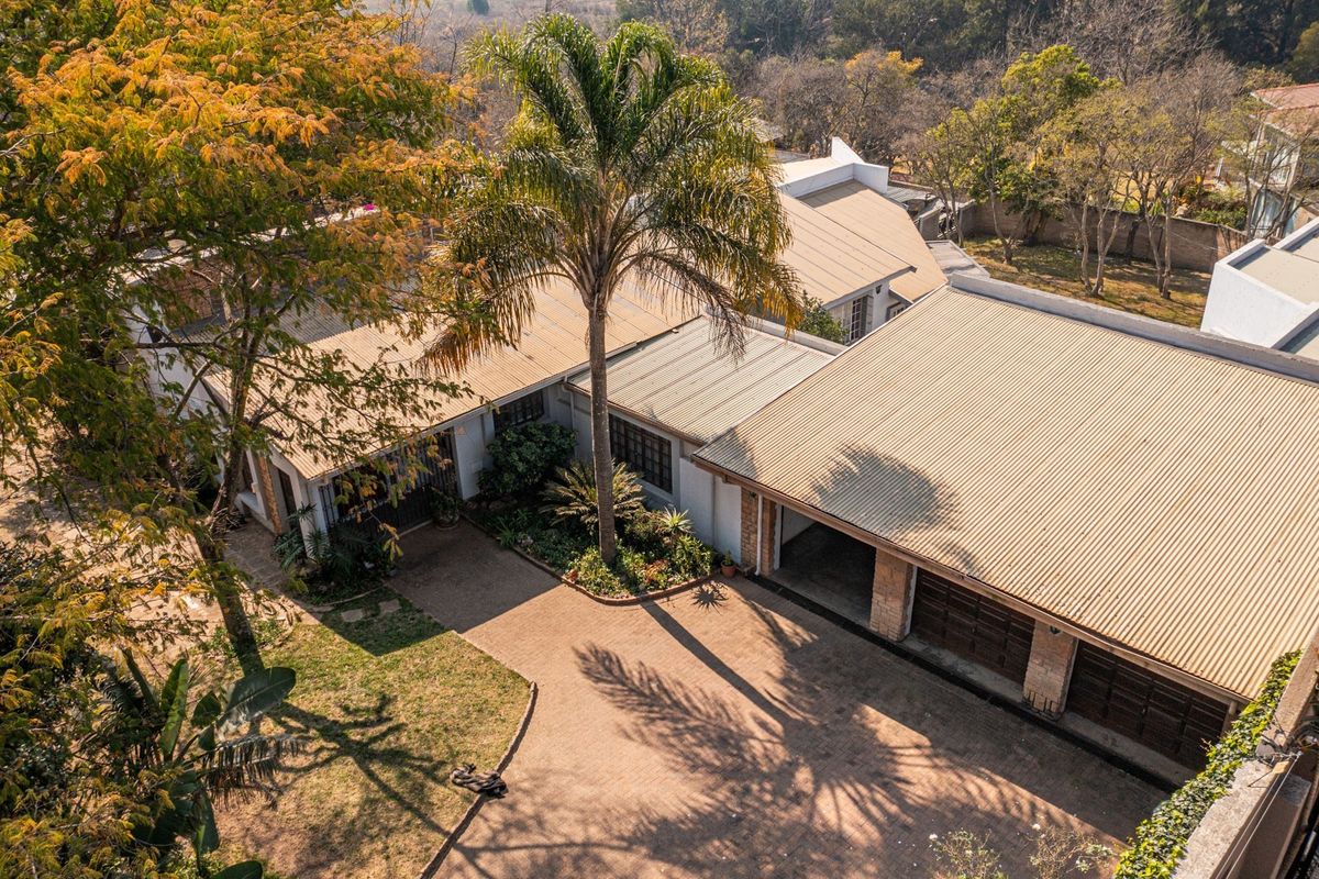 Aerial view of the property showcasing the main house, paved driveway, multi-car garage, and established garden surroundings.