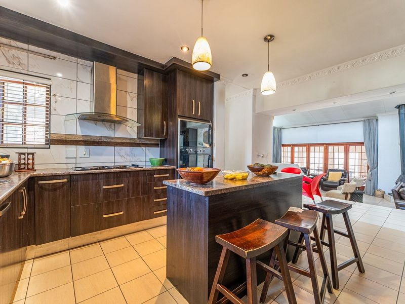 Open-plan kitchen featuring dark wood cabinetry, granite countertops, and integrated appliances, flowing seamlessly into a bright living area with tiled flooring.