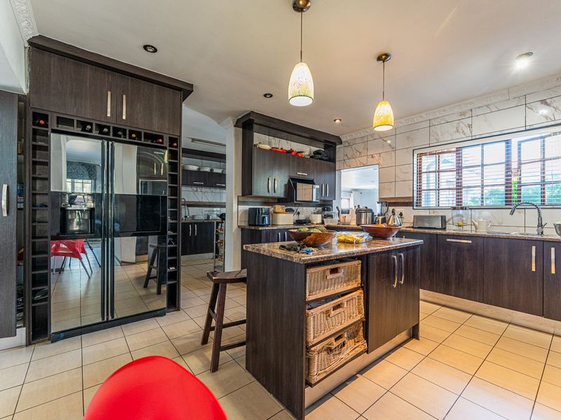 Modern kitchen featuring dark wood cabinetry, stone countertops, a central island, and tiled finishes, offering a functional and well-lit cooking space.