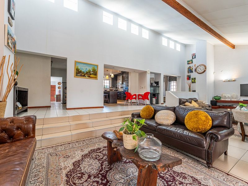 Spacious open-plan living area featuring high ceilings with exposed timber beams, clerestory windows, and a split-level layout connecting to the kitchen.