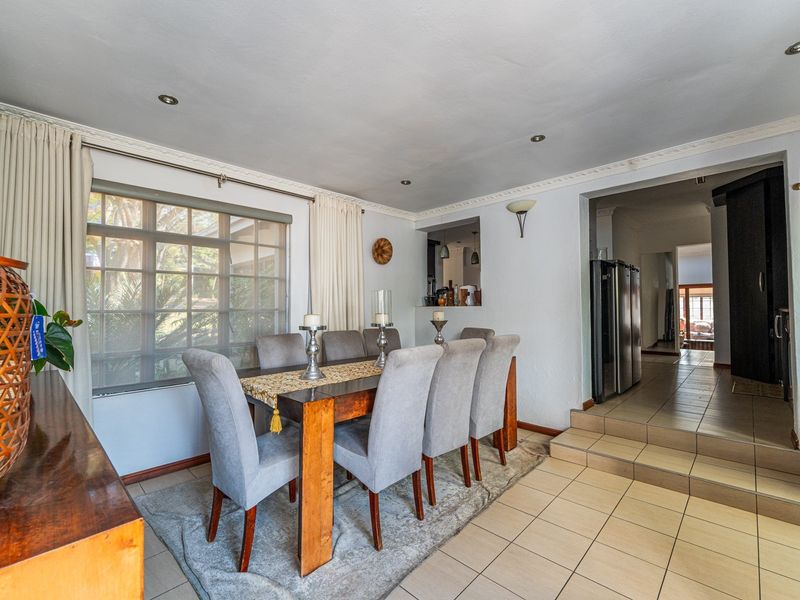 A dining room featuring tiled flooring, recessed lighting, and a pass-through window connecting to the kitchen area, with a stepped transition to the hallway.