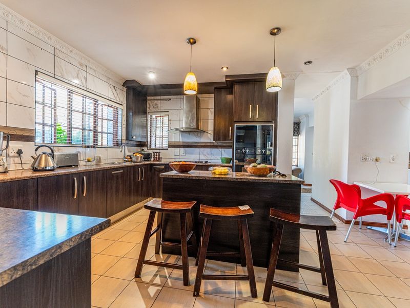 A well-appointed kitchen featuring dark wood cabinetry, granite countertops, a central island, and modern stainless steel appliances with tiled flooring.