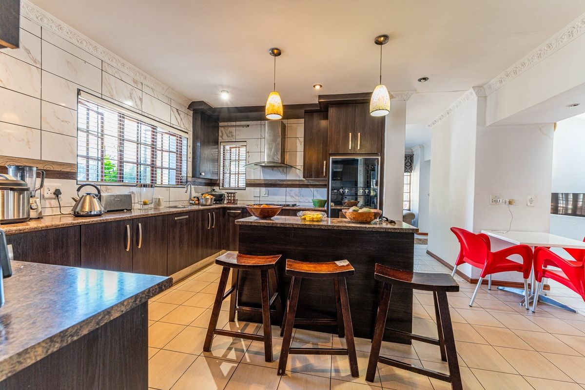 A well-appointed kitchen featuring dark wood cabinetry, granite countertops, a central island, and modern stainless steel appliances with tiled flooring.