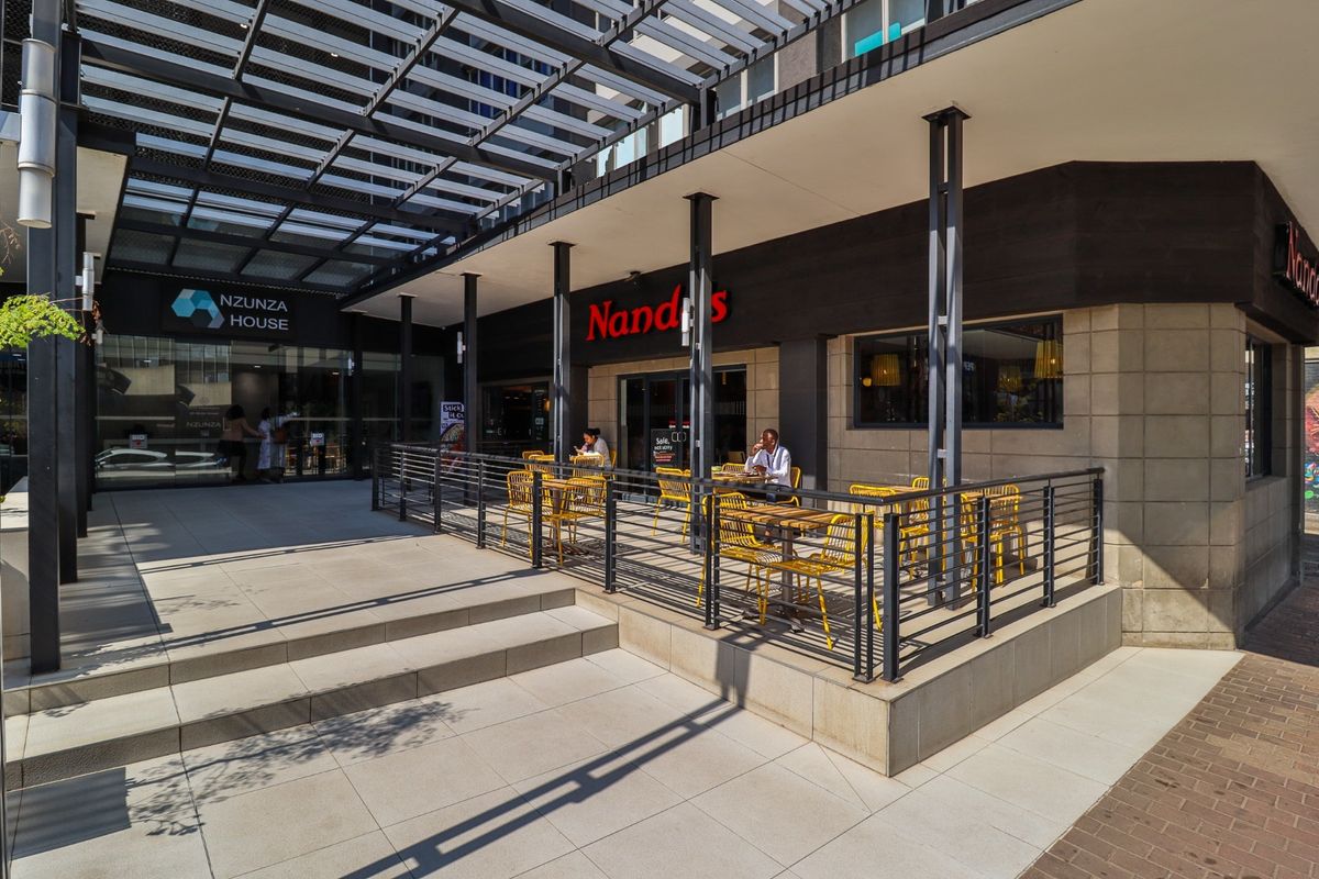 A modern commercial outdoor seating area featuring a metal pergola, steel structural columns, and tiled flooring, providing a well-maintained exterior space for patrons.