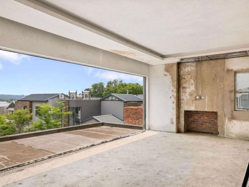 An unfinished living area featuring an exposed brick fireplace, concrete floors, and a large opening leading to an outdoor balcony with neighborhood views.