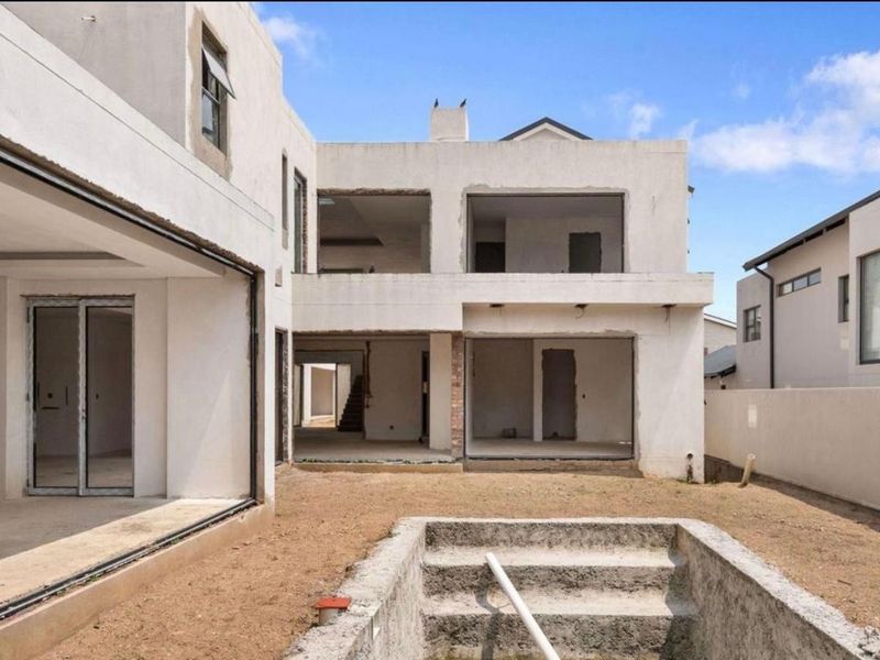 Rear view of a double-story residential property under construction, featuring an unfinished swimming pool shell and open-plan living areas awaiting final finishes.