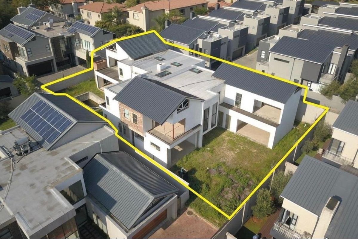 Aerial view of a modern residential property featuring a multi-level structure with metal roofing, balconies, and an undeveloped garden area within a secure estate.