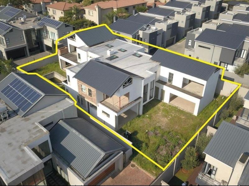 Aerial view of a modern residential property featuring a multi-level structure with metal roofing, balconies, and an undeveloped garden area within a secure estate.