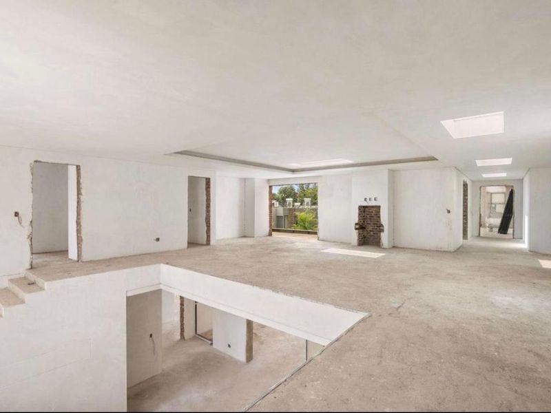 A spacious, open-plan interior in shell condition, featuring skylights, a fireplace, and an open staircase, offering a blank canvas for renovation.
