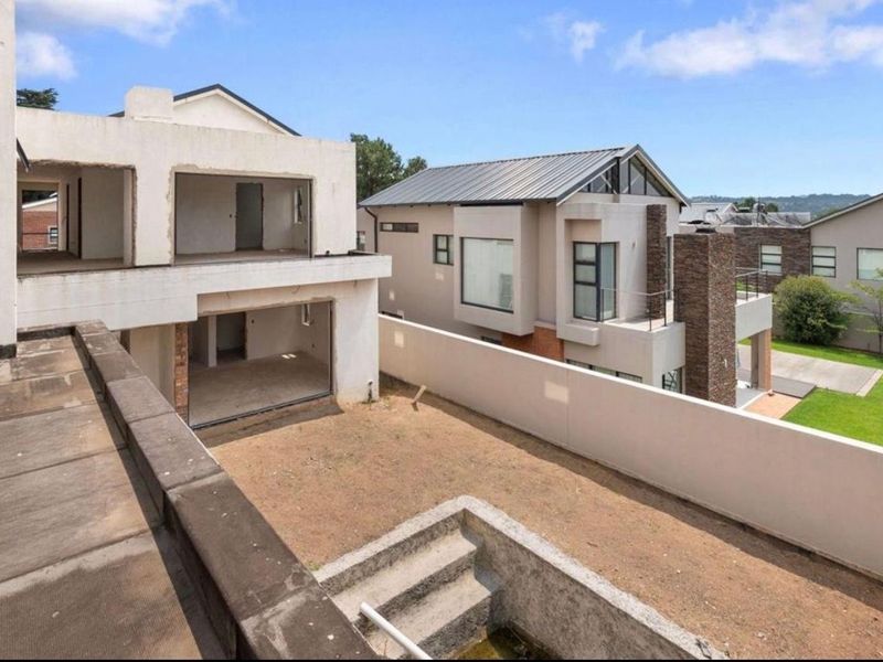 Rear view of an unfinished residential property showing a concrete boundary wall, staircase, and open-plan structural shell awaiting completion.