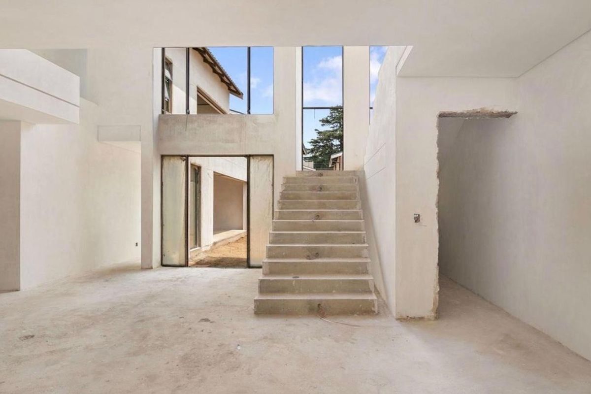 An expansive, double-volume living area currently under construction, featuring a central concrete staircase, large windows, and direct access to the rear exterior.