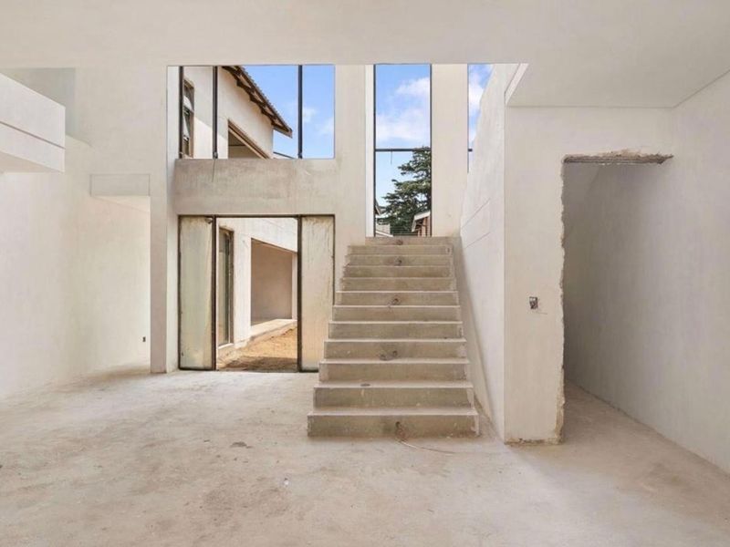 An expansive, double-volume living area currently under construction, featuring a central concrete staircase, large windows, and direct access to the rear exterior.