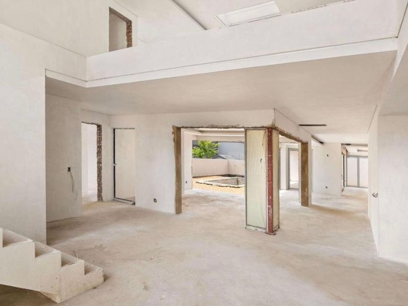 An expansive open-plan living area currently under construction, featuring a concrete staircase, mezzanine level, and structural steel elements ready for final finishes.