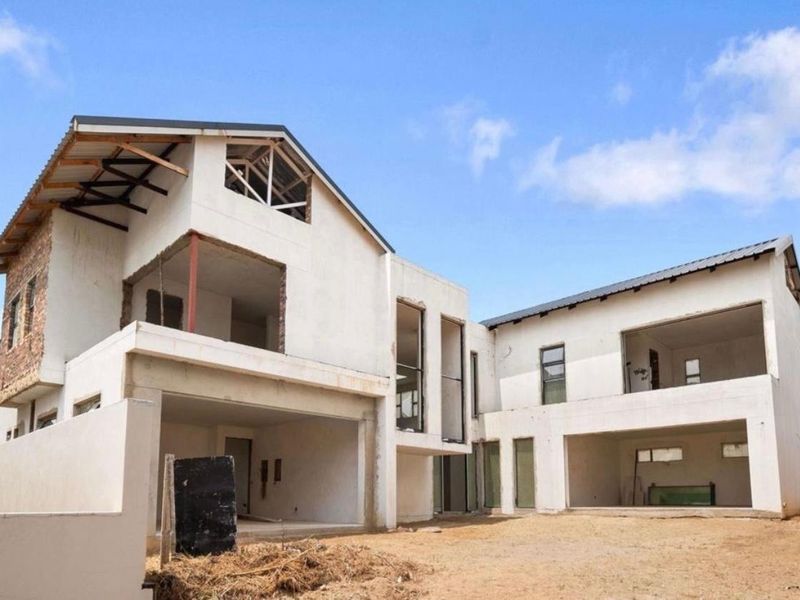A rear view of a large residential property currently under construction, featuring exposed structural framing, unfinished masonry, and open balcony spaces.