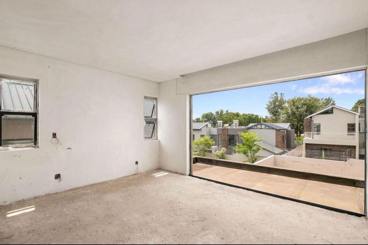 An empty, unfinished bedroom featuring large sliding glass doors that open onto a balcony, offering views of the surrounding residential area.