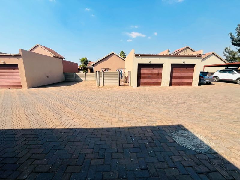 A paved driveway area featuring multiple garage units with roll-up doors and perimeter walling in a townhouse complex setting.
