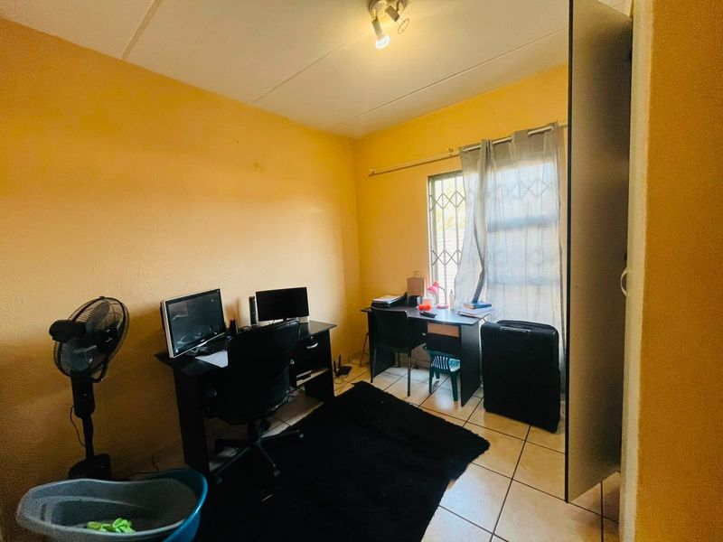 A functional office space featuring tiled flooring and a window equipped with security bars, providing natural light and a secure environment.