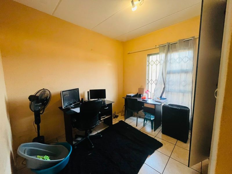 A functional office space featuring tiled flooring and a window with security bars, offering a blank canvas for potential renovation or home office setup.