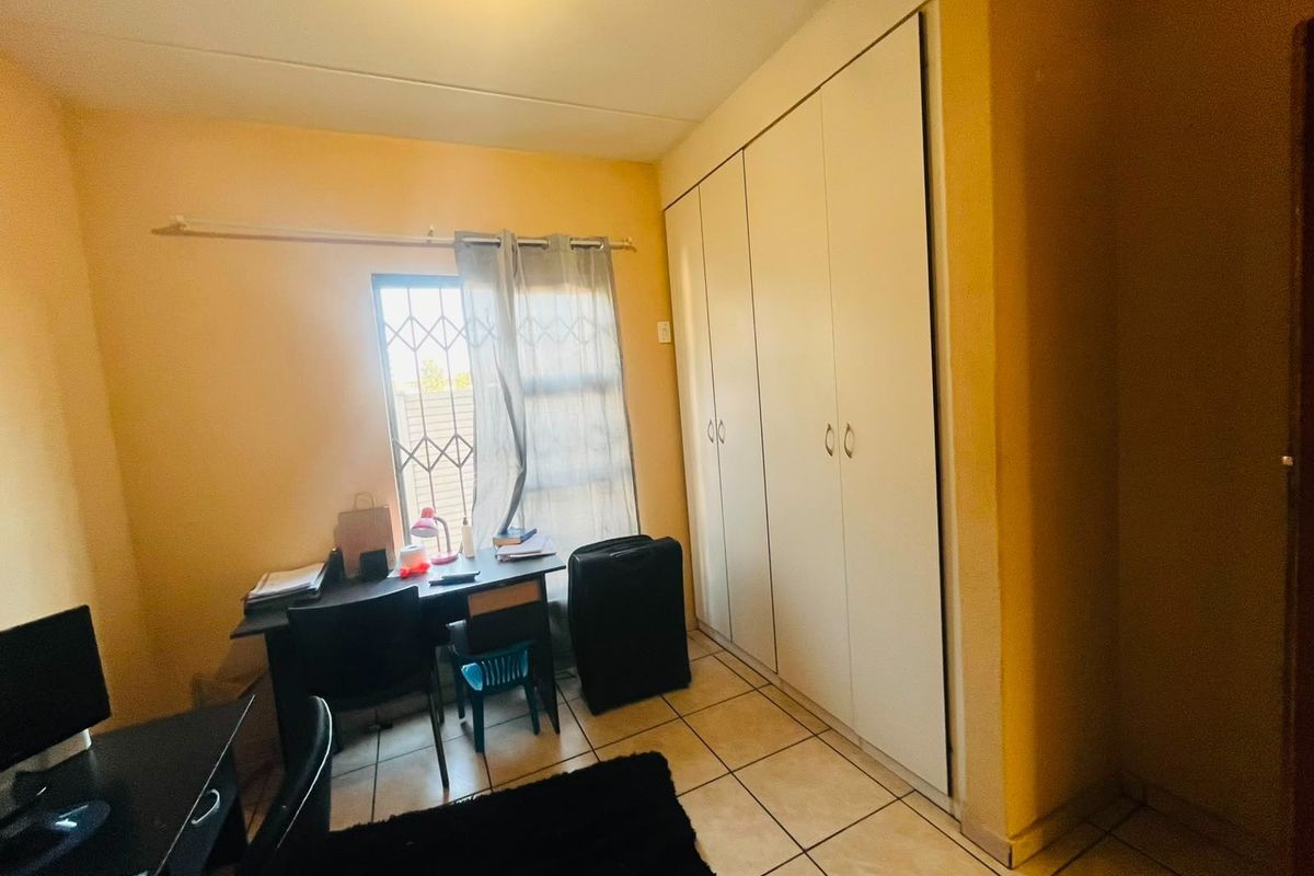 A functional bedroom featuring tiled flooring, built-in cupboards for storage, and a window fitted with a security gate.