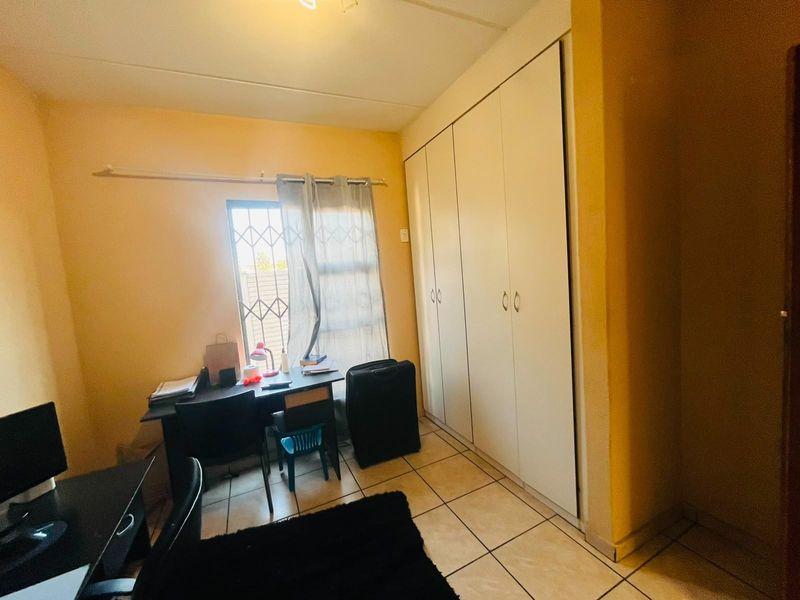 A functional bedroom featuring tiled flooring, built-in cupboards for storage, and a window fitted with a security gate.