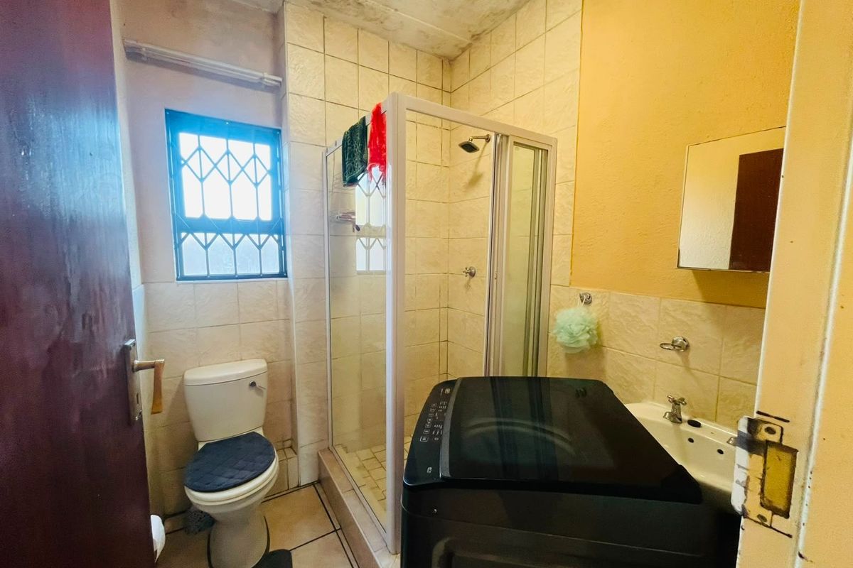A compact bathroom featuring a shower enclosure, toilet, and washbasin, with visible signs of ceiling water damage and dated finishes requiring maintenance.