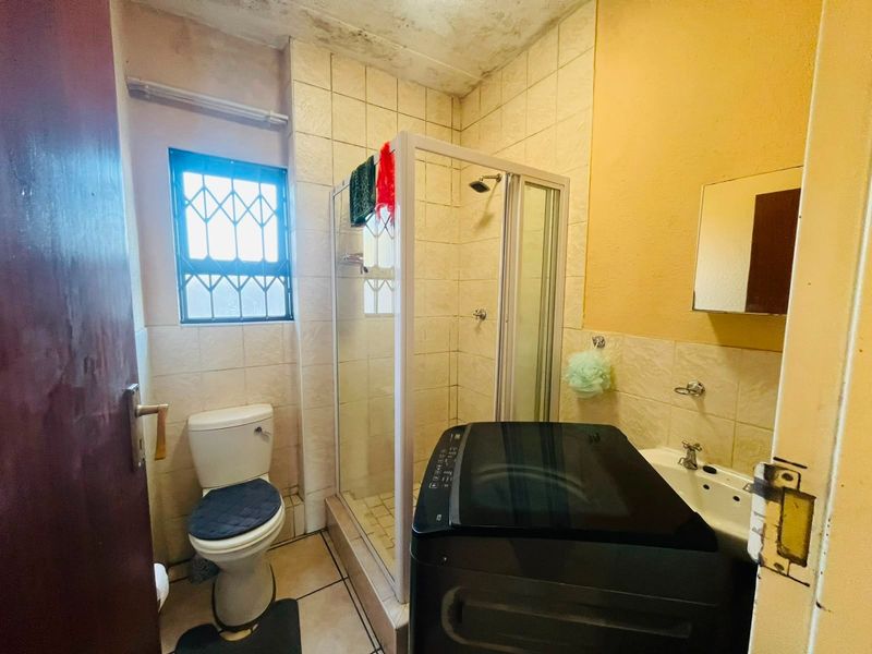 A compact bathroom featuring a shower enclosure, toilet, and washbasin, with visible signs of ceiling water damage and dated finishes requiring maintenance.