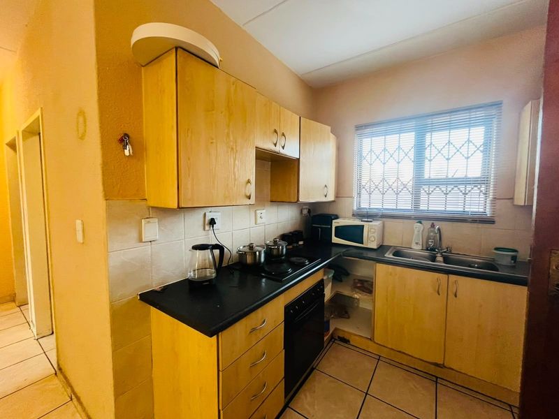 A compact kitchen featuring light wood-tone cabinetry, dark laminate countertops, a built-in oven and hob, and tiled flooring with security bars on the window.