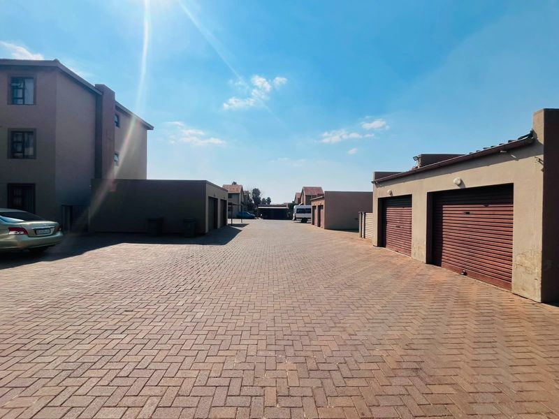 A view of the townhouse complex driveway featuring multiple garage units with roller shutter doors and paved access.
