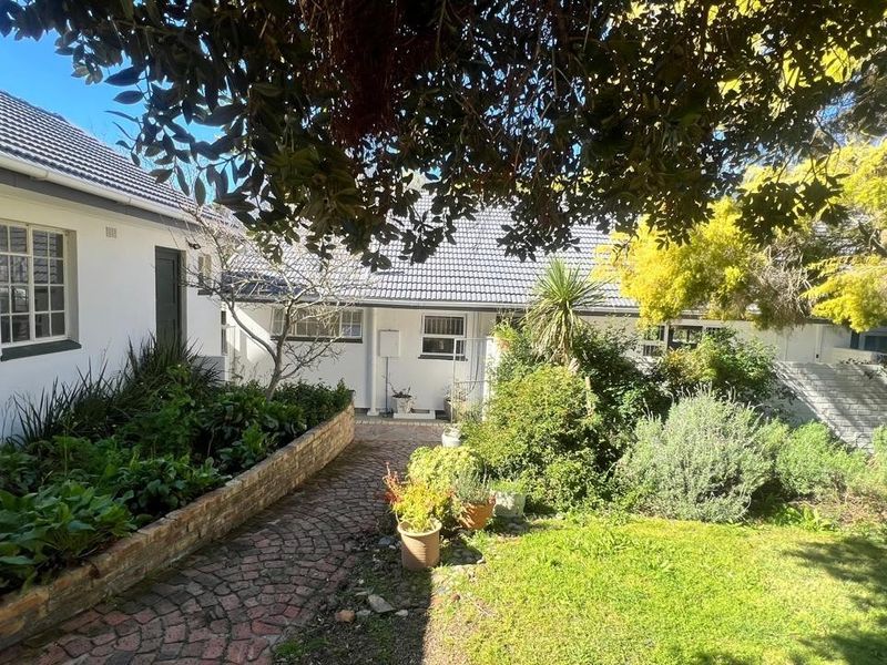 A view of the rear exterior of the house featuring a brick paved pathway, raised garden beds, and established landscaping.